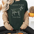 Person wearing a dark green t-shirt with a goat graphic and text, sitting in a cozy indoor setting.