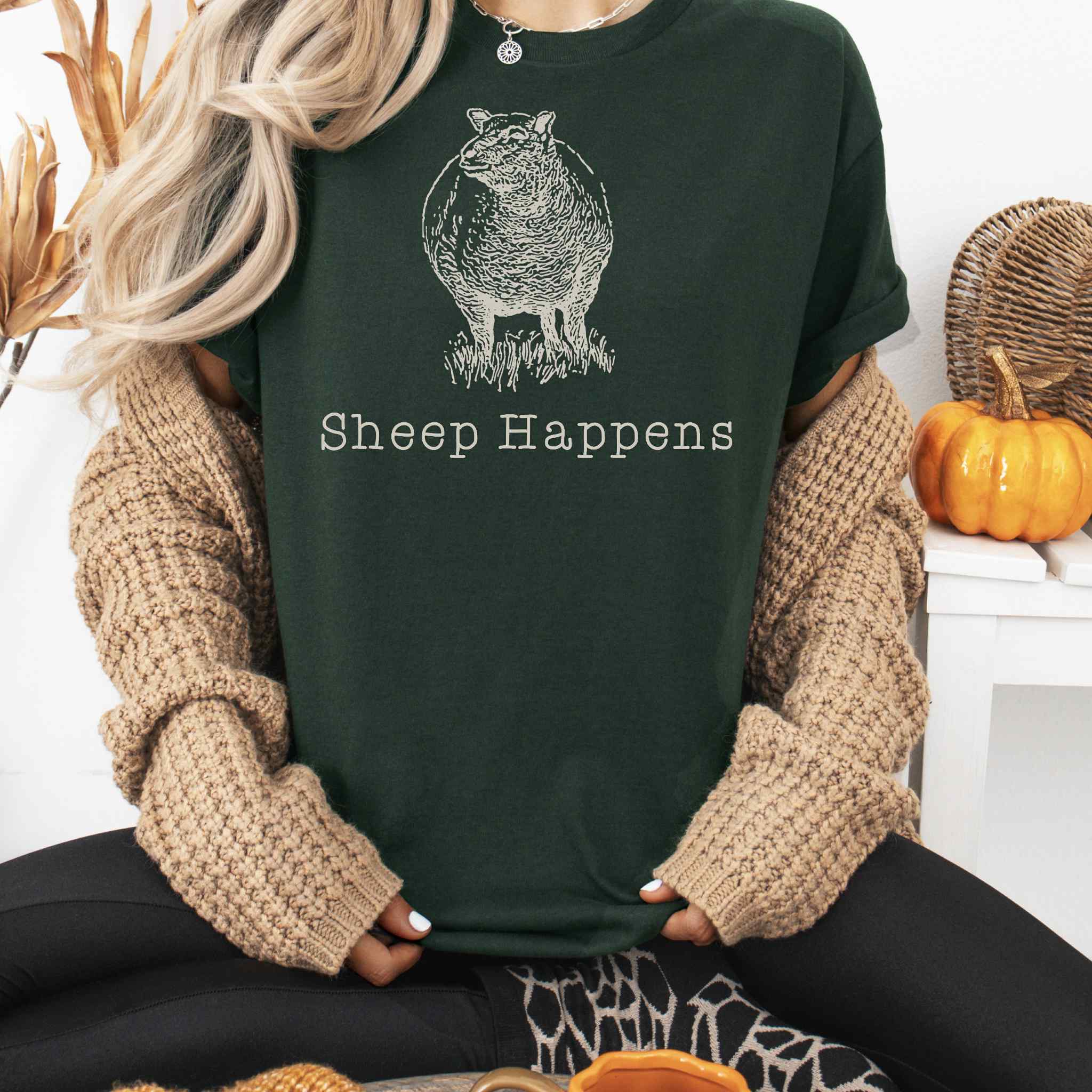 Person wearing a dark green t-shirt with 'Sheep Happens' text and graphic, sitting in a cozy indoor setting.